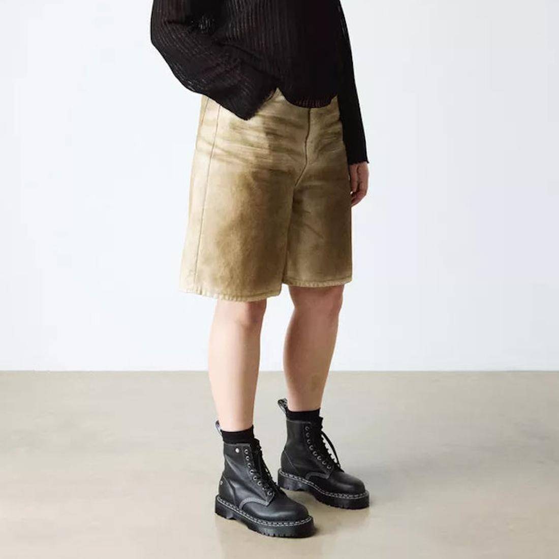 A person wears a black long-sleeve top, tan knee-length shorts, black socks, and Dr Martens Bex 1460 WDS White Stitching Black Boot Sendal, standing against a plain light-colored background., 50363, 50364, 190665803068, 190665803075, 190665803099, 50369, 