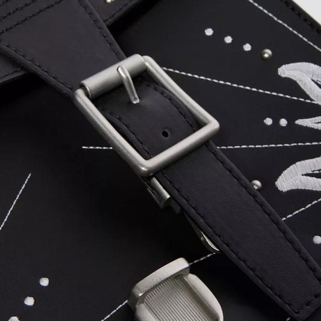 Close-up of the Dr Martens Mini Genix Nappa Solar Flare Leather Backpack in black, showcasing its black leather strap with a silver buckle and white embroidered patterns., 190665739695