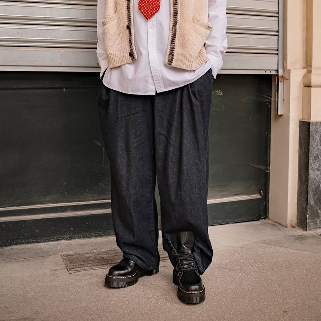 A person is seen outdoors in loose dark pants and black Dr Martens - Jadon Polished Smooth Boot 8 up, styled with a white shirt, cream sleeveless sweater, and red tie. The cropped photo shows only their lower half., 883985578883, 883985578890, 88398557890