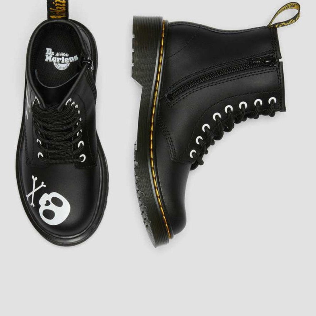 The Dr Martens Kids 1460 Junior X Bones With Zip (last size UK 10) features black boots with a white skull and crossbones on the toe, black laces, side zipper, and yellow sole stitching, shown on a light gray background., 190665457018, 190665457032, 19066
