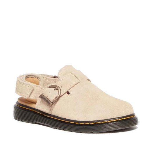 The Dr Martens Kids Junior Jorgie Bronx Suede Mule Sandal in Light Tan features a closed toe, open heel, adjustable buckle strap, and a black sole with yellow stitching details.