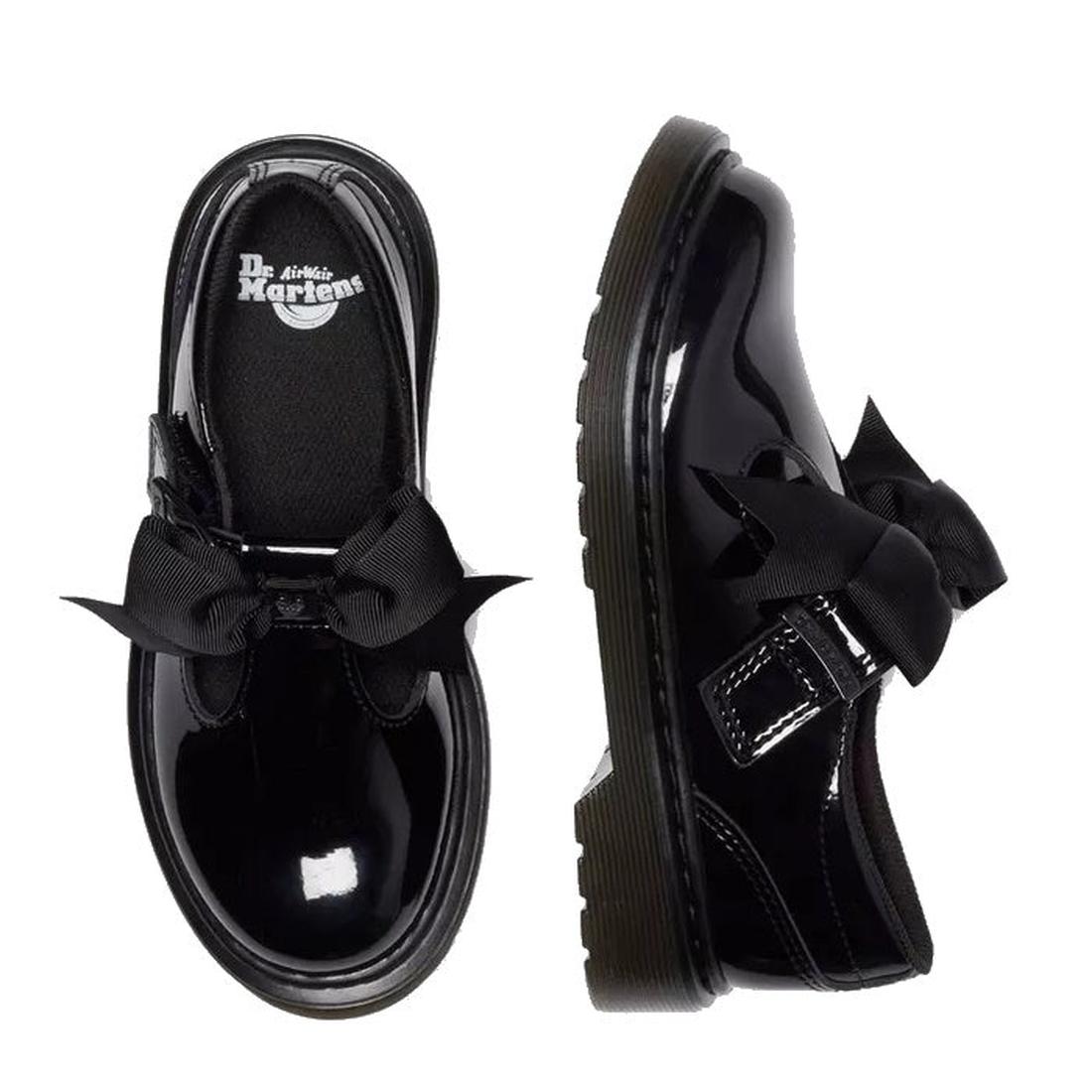 A flay lay of a pair of Dr Martens Kids Polley Bow Black patent leather shoes with bows on a white background. The right foot top down showing the Dr Martens ogo on the footbed, The left foot showing the outer.,
190665761818,
190665761832,
190665761856,
1
