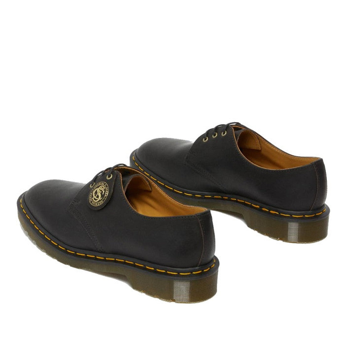 A pair of Dr Martens Made In England Oil Leather 1461 3 Eye Shoes in black, featuring yellow stitching, brown lining, and a circular logo tag on one eyelet—crafted with vintage oiled leather., 190665425826, 190665425895, 22989, 22986, 190665425833, 22987,