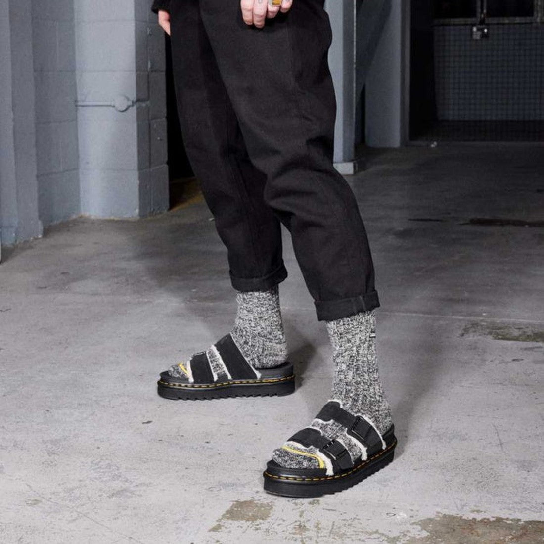 Person wearing grey wool socks and Dr Martens - Myles Black Suede Fur Lined Sandal CLEARANCE, standing on a concrete floor indoors. Their black pants are rolled at the cuffs. Only the lower half of their body is visible., 25879, 25880, 190665493030, 19066