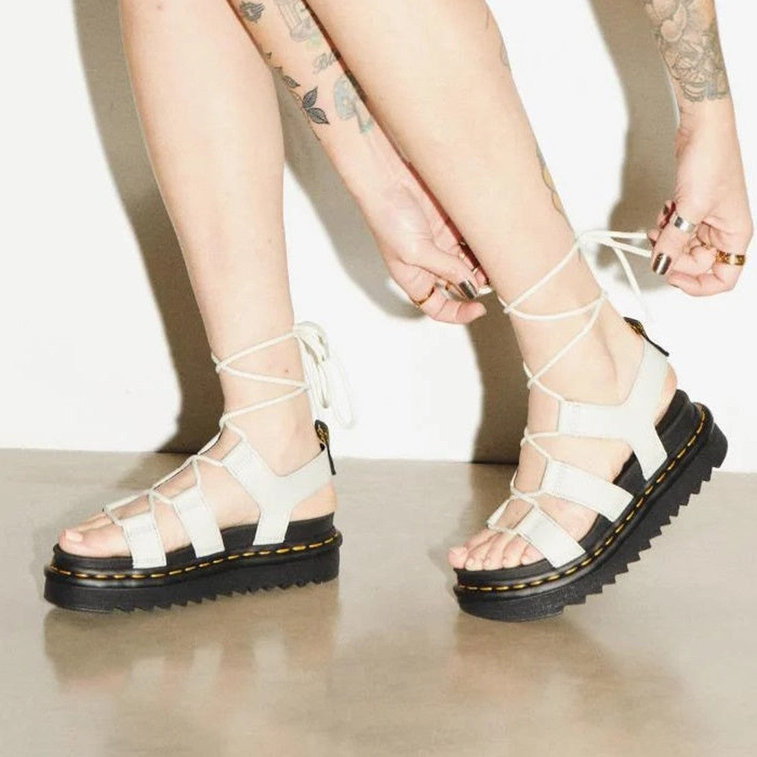 A friendly adult ties the white lace-up straps of Dr Martens Nartilla Gladiator Sandal Smoked Mint Athena, with a sturdy black sole and bright yellow stitching.  ksnz, 190665644791, 190665644807, 190665644814, 190665644838, 190665644845