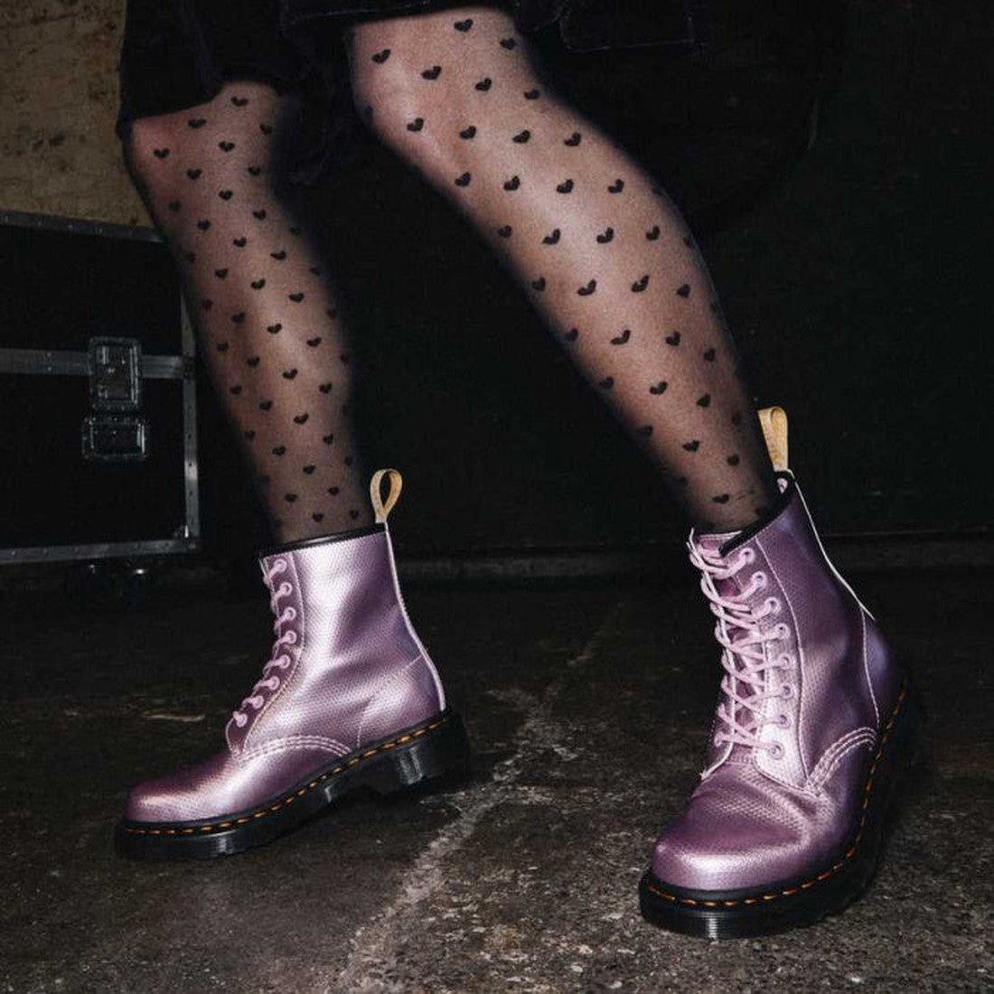 A person wearing sheer black heart-patterned tights and Dr Martens Vegan 1460 Pink Lavender Alumix Hex Emboss boots stands on a concrete floor., 190665418767, 190665418774, 190665418781, 190665418798, 190665418804, 190665418811, 190665418828, 21879