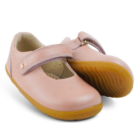 The Bobux Step Up Mary Jane Delight Dusk Pearl Pink 728426 is a pair of children's premium leather shoes with tan rubber soles and a hook-and-loop strap. One shoe stands upright, the other tilts to show the sole.