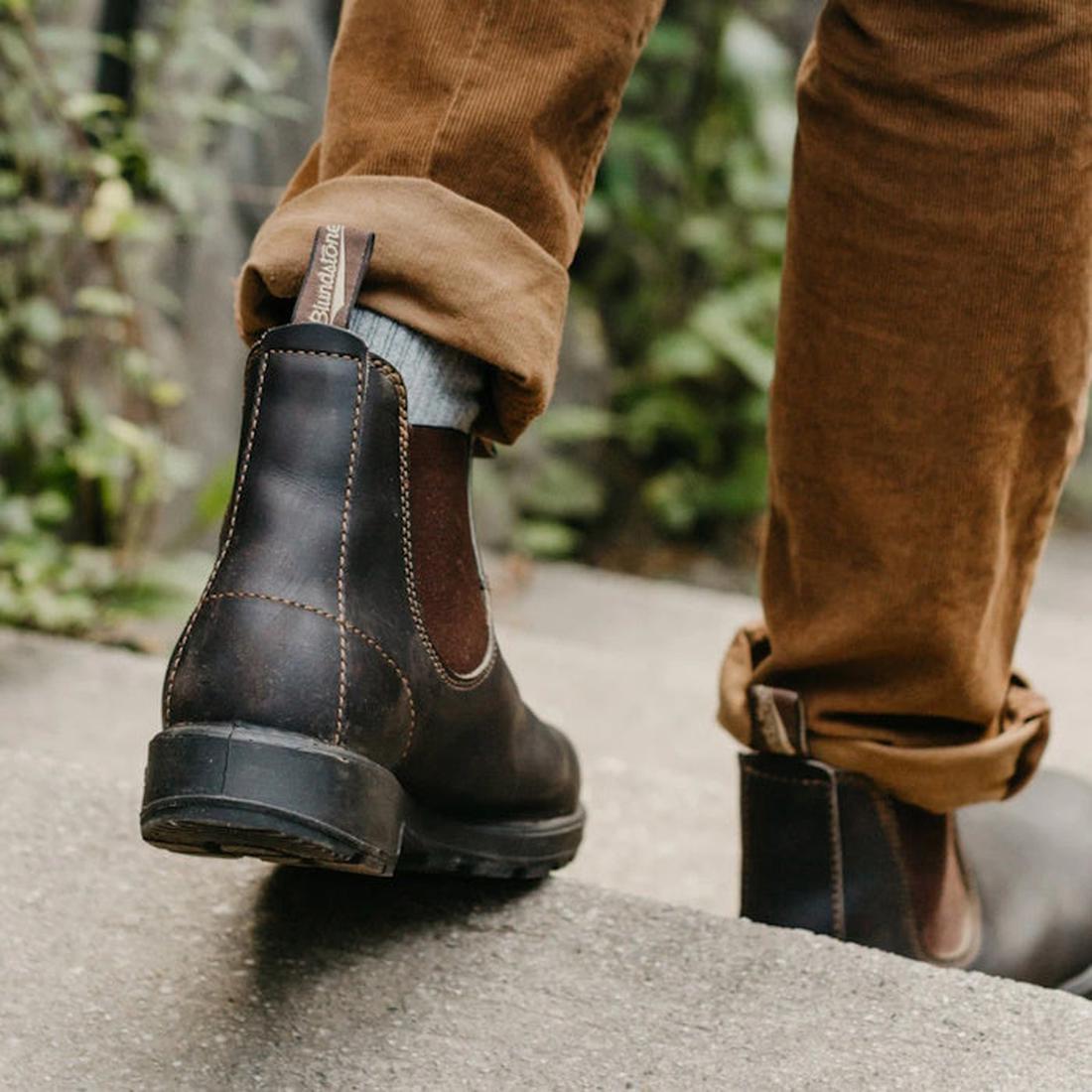 a models feet wearing brown blunstone 500 leather boots, The shot is from behind and the person is walking down a step. It shows the heel and back of the boot of the left foot and the side with elastic gusset and heel of the right foot.
9315891068116,
931