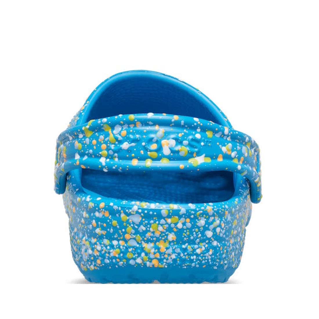 The Crocs Kids - Youths Classic Clog K Paint Splatter Print Blue Multi is a blue youth clog with a back strap, featuring a white, yellow, and light blue splatter print, shown from the rear on a white background., 198445210136, 198445210143, 198445210150, 