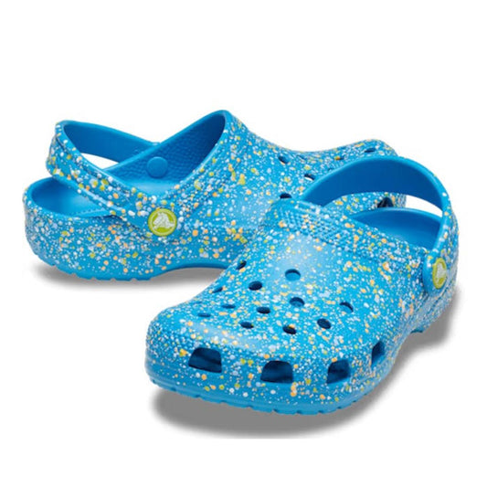The Crocs Kids - Toddlers Classic Clog K Paint Splatter Print Blue Pink Multi features a blue paint splatter design with yellow and white accents, ventilation holes on top, and a heel strap for comfort in lightweight kids' shoes.