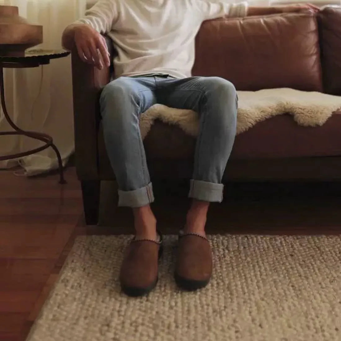 A parent in rolled-up jeans and EMU NZ Emu Platinum Outback Scuff Chestnut Sheepskin Slippers unwinds on a family sofa, cozy and safe.  ksnz