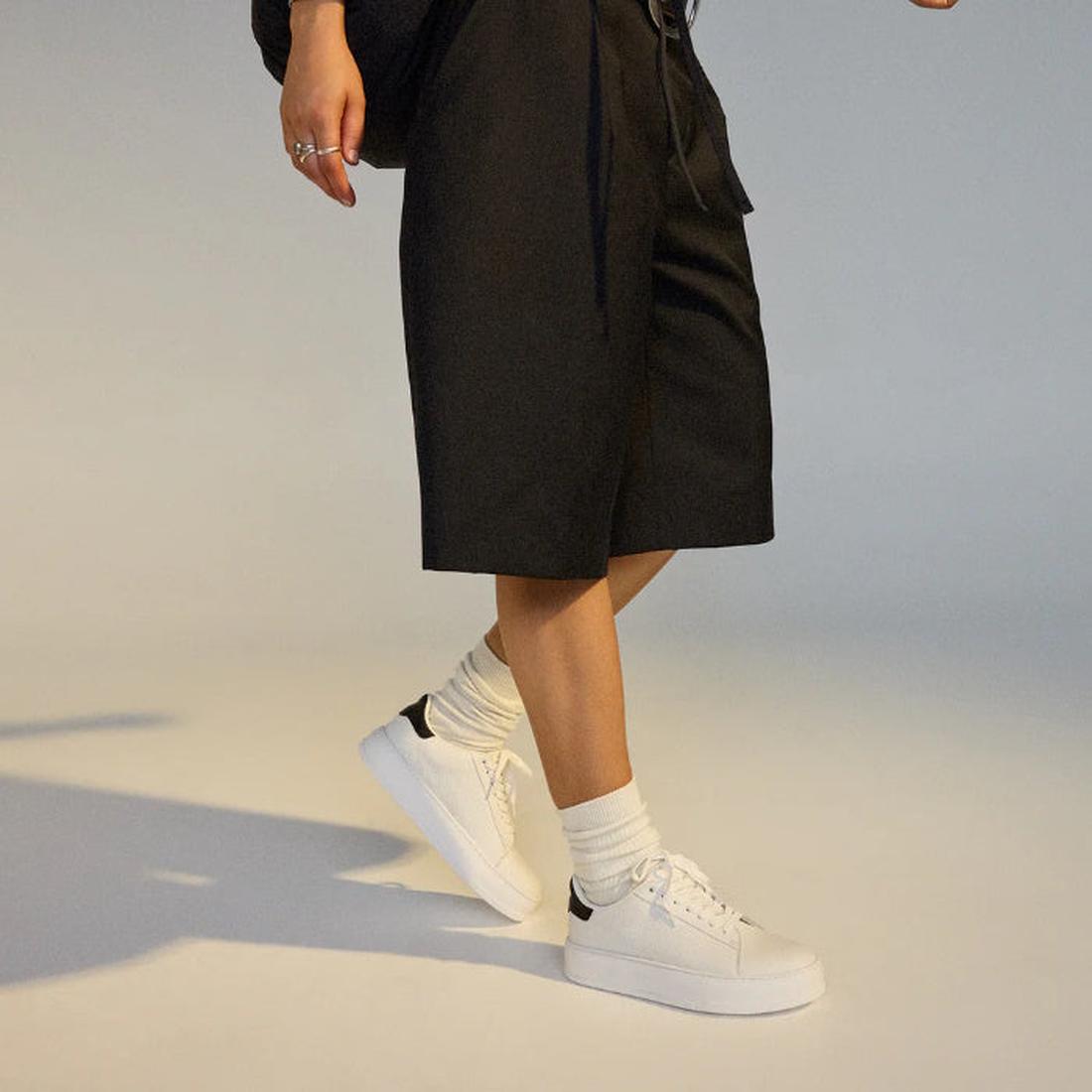 Person in a wlaking poise wearing a black skirt, white rollie club court lace up sneakers, and socks on a neutral background.,
9781760790097,
9781760790103,
9781760790110,
9781760790127,
9781760790134,
9781760790141,, 9781760790097, 9781760790103, 9781760
