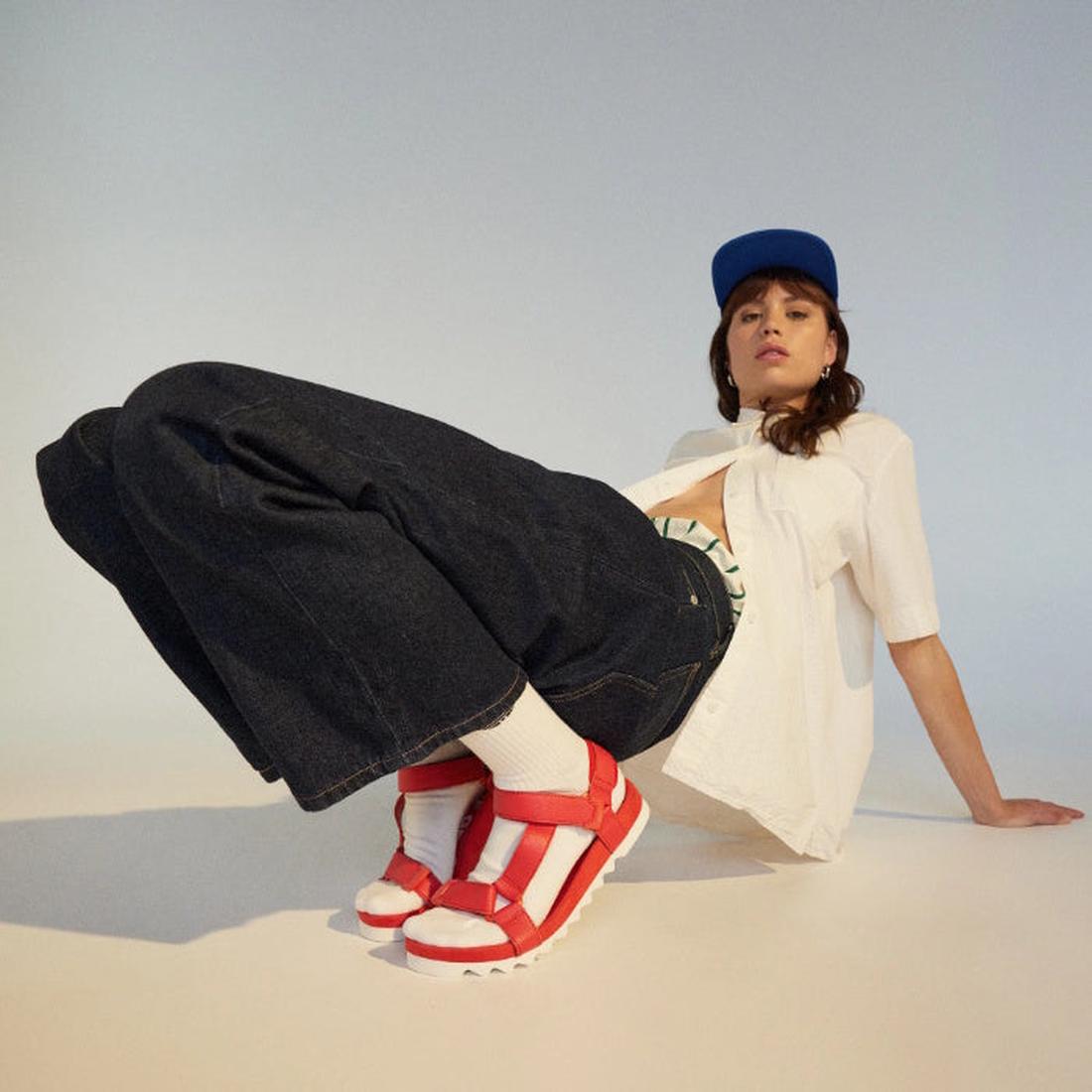 Smiling in wide jeans and a white tee, she relaxes in comfy, easy-on Rollie Womens Sandal Tooth Wedge Fiesta Red with sturdy sole.  ksnz, 9781760776053, 9781760776060, 9781760776077