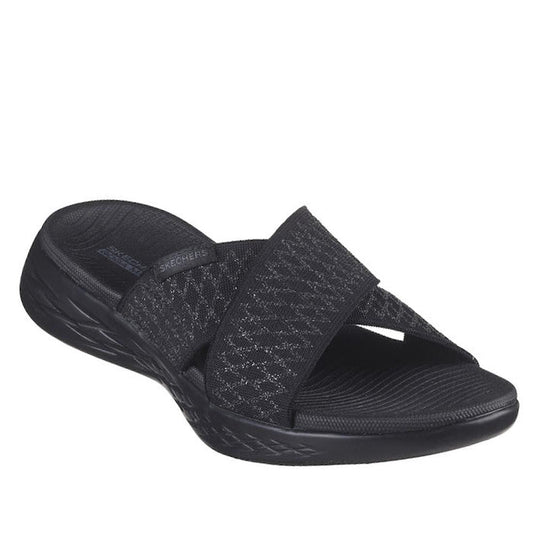 The Skechers On The Go 600 Slide Enchanted Black is a women's sandal with two wide, crisscross fabric straps, a textured sole, slightly raised heel, and Goga Mat comfort footbed for all-day wearability.
