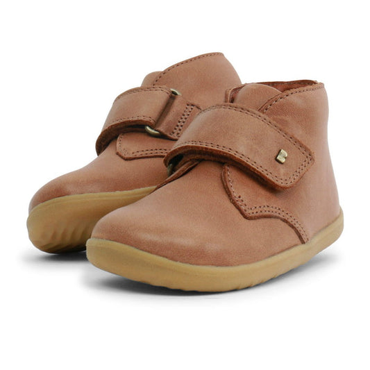 The Bobux Step Up Desert Boot Caramel 724820A is a pair of light brown leather toddler boots with rubber soles and wide velcro straps, displayed side by side on a white background.