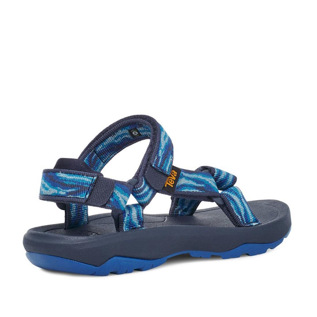 The Teva Kids K Hurricane XLT2 Wave Mood Indigo is an outdoor sandal with navy and blue adjustable recycled plastic straps featuring a wave pattern, a rugged sole, and a small orange logo tag for added color., 196565099884, 196565099938, 196565099907, 196